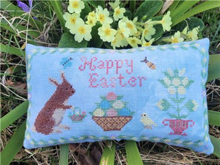 Cross-stitched Easter pillow with 'Happy Easter' text, a rabbit, and flowers on a grass background.