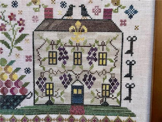 Cross-stitched house with decorative elements on a white background