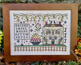 Framed cross-stitched sampler with house, alphabet, and floral patterns.