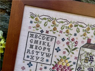 Framed cross-stitched sampler with floral patterns and alphabet letters.