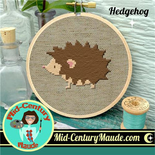 Cross-stitched hedgehog design in an embroidery hoop with 'Mid-Century Maude' branding.