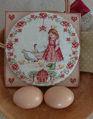 Decorative scene with a cross-stitched design of a girl and chick on a wooden surface.