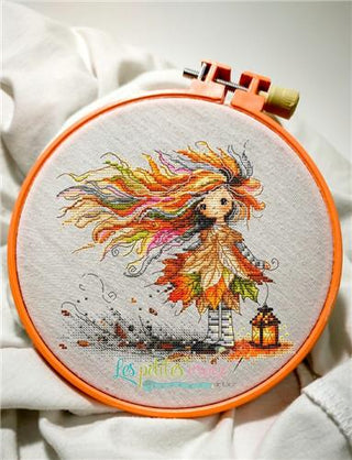Embroidery hoop with cross-stitched design of a girl with colorful hair and a lantern on a white fabric background.