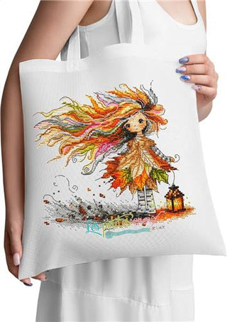Cross-stitched design of a woman with autumn-themed hair and leaves, standing next to a lantern on a textured fabric background.