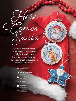 Christmas-themed craft pattern cover featuring embroidered Santa and Rudolph ornaments and a blue star ornament arranged on a red Santa hat with white faux fur, red beads, and a dark wood background. Large text reads 'Here Comes Santa' with a list of included designs and stitch names.