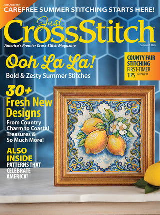 Magazine cover of 'Just Cross Stitch' with a cross-stitched lemon design on a blue geometric background.