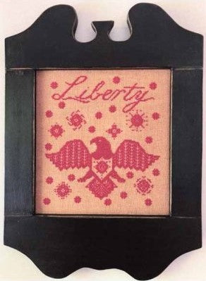 Monochrome red cross stitch featuring the word ‘Liberty’ above a stylized American eagle surrounded by geometric folk-art motifs, framed in black.