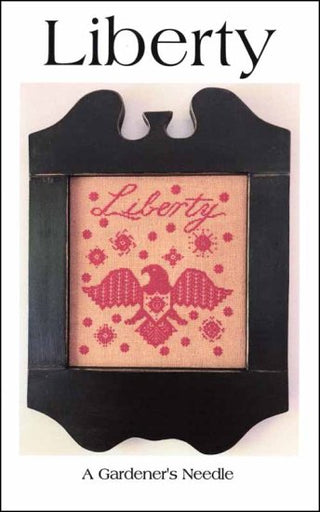 Monochrome red cross stitch featuring the word ‘Liberty’ above a stylized American eagle surrounded by geometric folk-art motifs, framed in black.