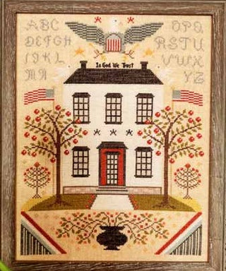 Sampler-style cross stitch design featuring a colonial house, alphabets, trees, and American flags with the phrase “Liberty and Union,” framed in a traditional style.