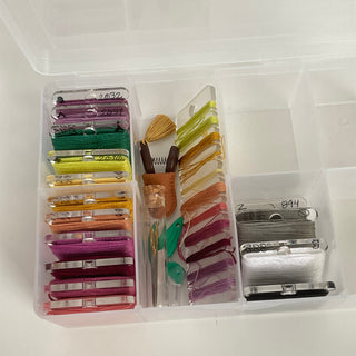 Set of embroidery threads and tools in a clear plastic container on a white background