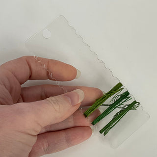 Hand holding green floral stems with a clear plastic packaging on a white background