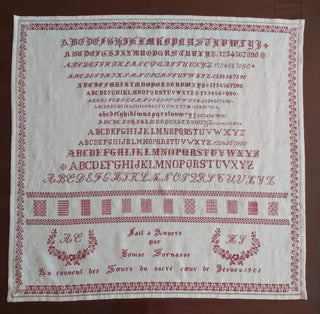 Antique-style red monochrome sampler cross stitch pattern featuring alphabets, numbers, decorative bands, and the name Louise Somasse dated 1903.
