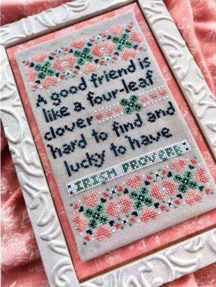 Cross stitch pattern with text and clover designs, framed in a white frame.