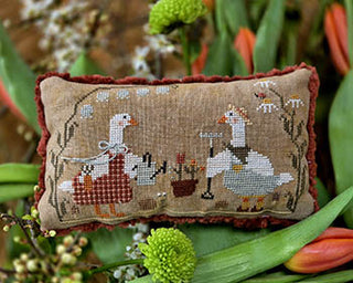 Decorative pillow with cross-stitched design of geese and flowers, surrounded by greenery.