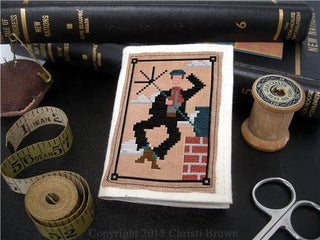 Bert the Chimney Sweep cross stitch design with sewing implements scattered around the background as decorationi against a black background.