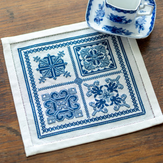 Embroidered blue and white placemat on a wooden surface with a cup and saucer.