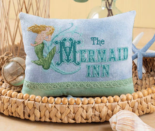Decorative pillow with mermaid design and 'The Mermaid Inn' text on a woven surface.