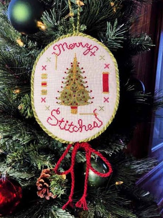 Cross-stitched Christmas ornament featuring a decorated tree, red “Merry Stitches” text around the circle, colorful buttons, and spool motifs, displayed hanging on a pine branch.