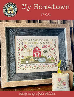 Cross stitch pattern depicting an American flag-themed design with a red barn, fence, and a white picket fence, titled 'My Hometown' by Annie Beez Folk Art.