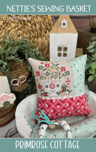 Nettie’s Sewing Basket cross stitch pattern by Primrose Cottage Stitches featuring a flower-filled sewing basket with scissors, thread spools, pincushion and stitching motifs.