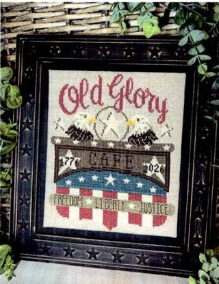Framed cross-stitched design of an American flag with 'Old Glory' text, surrounded by greenery.
