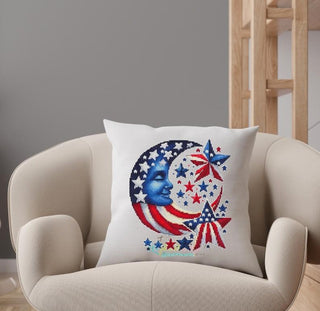 Decorative cross stitched pillow with a moon and star design on a beige armchair.