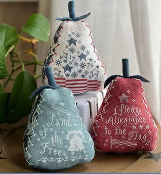 Three pear-shaped cross stitch designs with patriotic patterns and text including “Land of the Free” and “I Pledge Allegiance,” finished as decorative stuffed ornaments in red, white, and blue.
