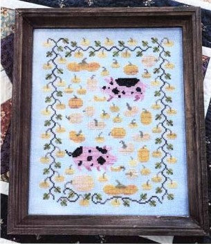 Cross-stitched design of cows and pumpkins on a light blue background, framed in dark wood.