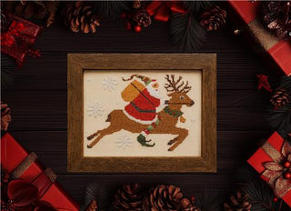 Framed cross-stitched picture of Santa Claus on a reindeer surrounded by Christmas decorations.