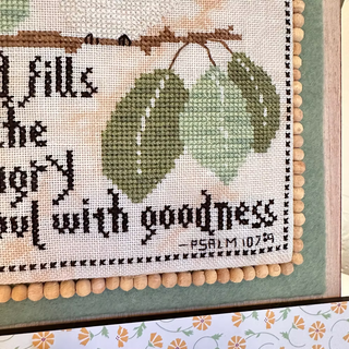 Cross-stitched piece with leaves and text on a fabric background