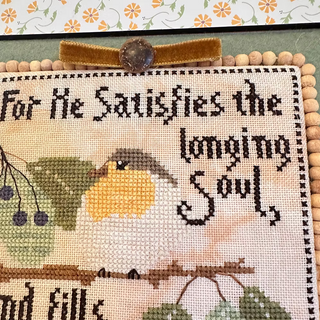Cross-stitched piece with a bird and text on a wooden frame.