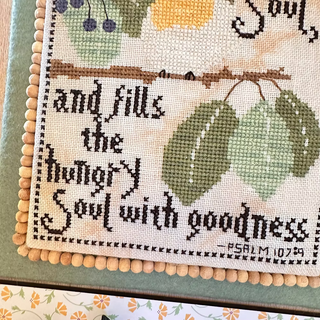 Cross-stitched text with green leaves and berries on a fabric background