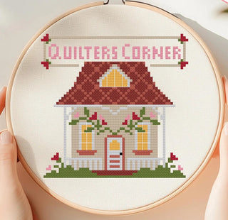 Embroidery hoop with a cross-stitched design of a house. Quilter's Corner' text.