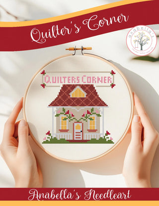 Cross-stitched design of a house in an embroidery hoop with 'Quilter's Corner' branding.