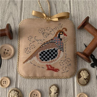 Cross Stitch square with a partridge design on a wooden surface with buttons and spools.