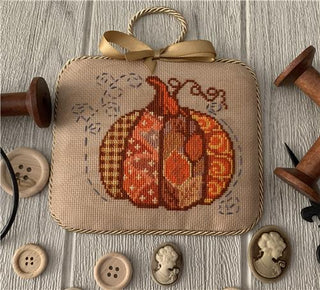 Decorative ornament with cross-stitched pumpkin design on a wooden surface with buttons and spools.