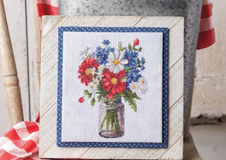 Cross-stitched floral design in a jar on a wooden frame with a red, white, and blue color scheme.