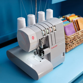 Singer sewing machine on a blue surface with spools of thread and fabric in the background.