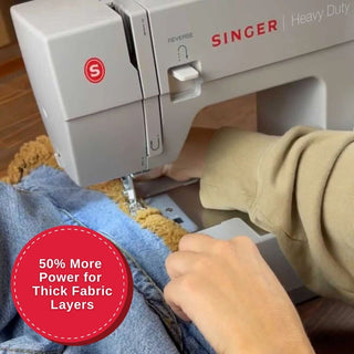 Singer sewing machine being used on thick fabric with a person's hand guiding the material.
