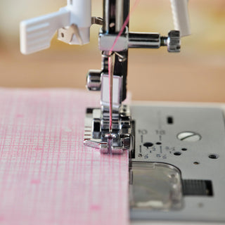 Close-up of a sewing machine needle threaded with pink thread on a blurred background