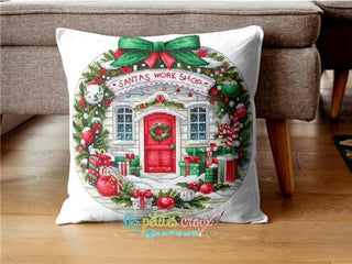 Decorative pillow with Santa's Workshop design on a wooden floor.