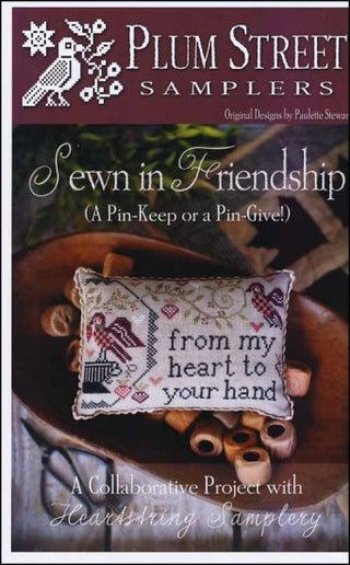 Cover of the 'Sewn In Friendship' cross stitch pattern booklet by Plum Street Samplers, featuring a white pillow with a embroidered message and floral design.
