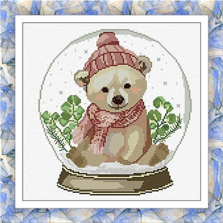 Cross-stitched design of a bear in a snow globe with a pink hat and scarf on a blue and white patterned background.