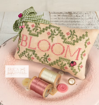 Decorative pillow with 'BLOOM' embroidery on a textured surface with spools of thread.