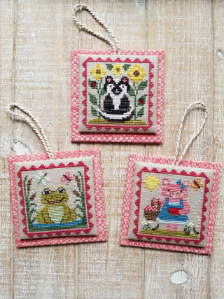 Three cross-stitched ornaments with animal designs on a textured fabric background.