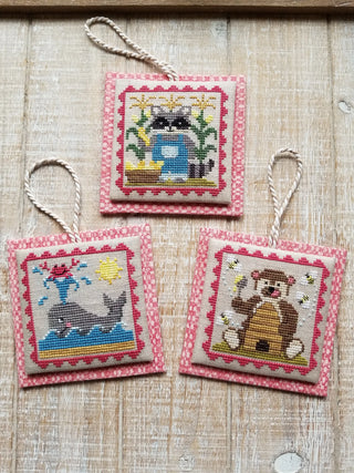 Three cross-stitched ornaments on a wooden surface