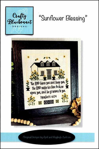Cross stitch pattern featuring a house surrounded by sunflowers and a blessing verse, finished as a framed design by Crafty Bluebonnet Designs.