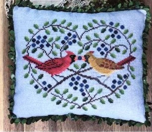 Cross stitched pillow with two birds on a branch design on a wooden surface