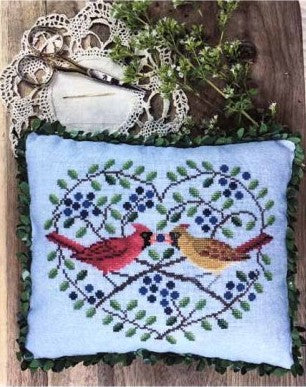 Small cross stitched pillow with foliage heart with two cardinals, one red and one yellow connected to each other in what looks to be a kiss, if birds did such a thing. ;) 