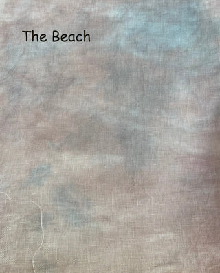 A close-up of a textured fabric with a mottled, tie-dye pattern in soft beige, gray, and light blue, with the text 'The Beach' printed in black in the upper left corner.
